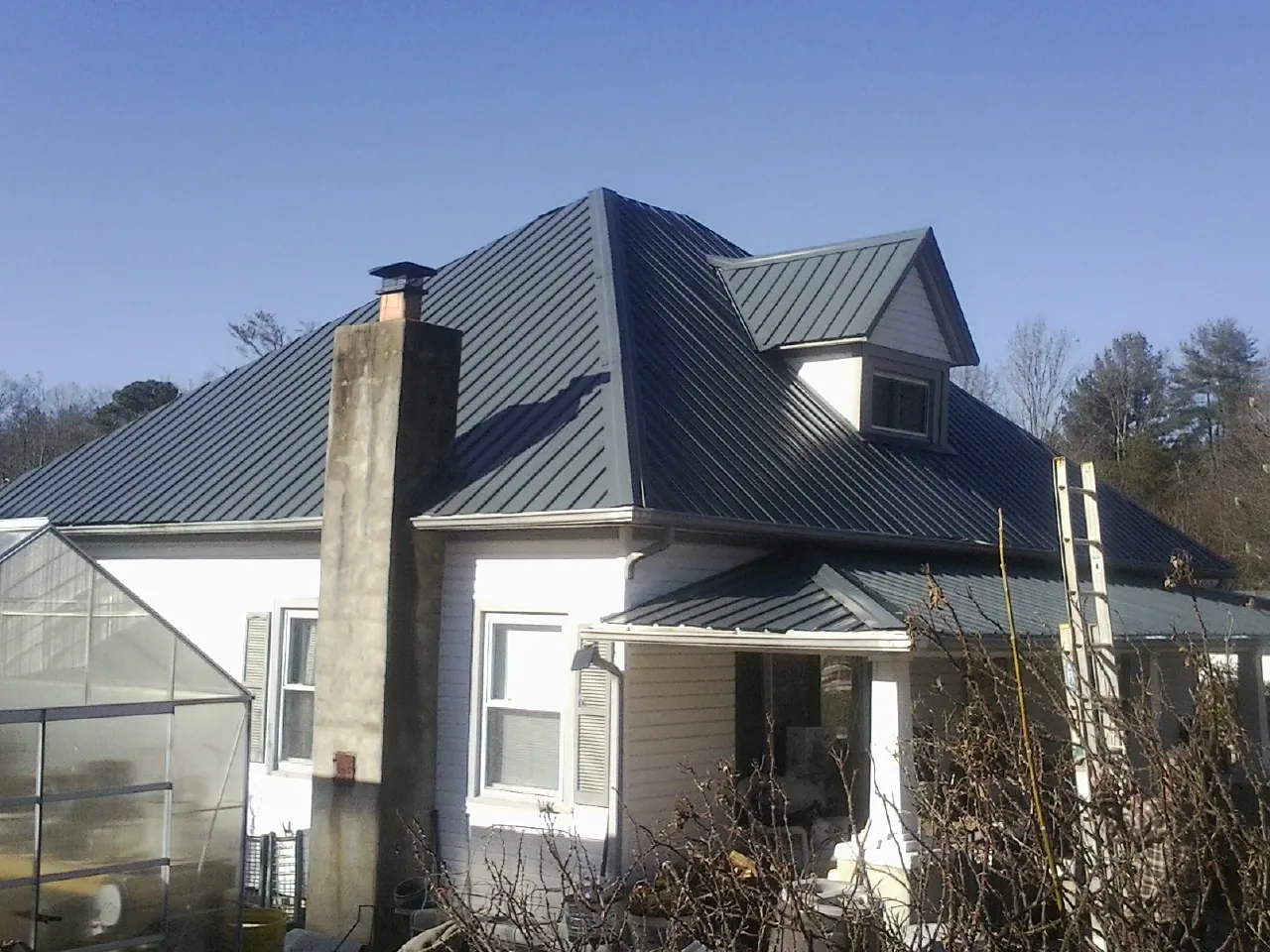 Dark blue standing seam metal roof on a white farmhouse with dormer — Slate & Tile Roof Repair by Roofing Brothers in Cross City