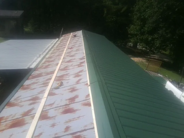 Old rusted panels beside newly installed green metal roofing — Wind Damage Roof Repair by Roofing Brothers in Cross City