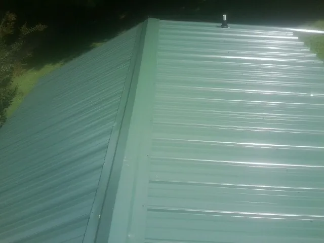New green metal panels meeting at the ridge of a roof — Flat Roof Repair work by our crew in Cross City