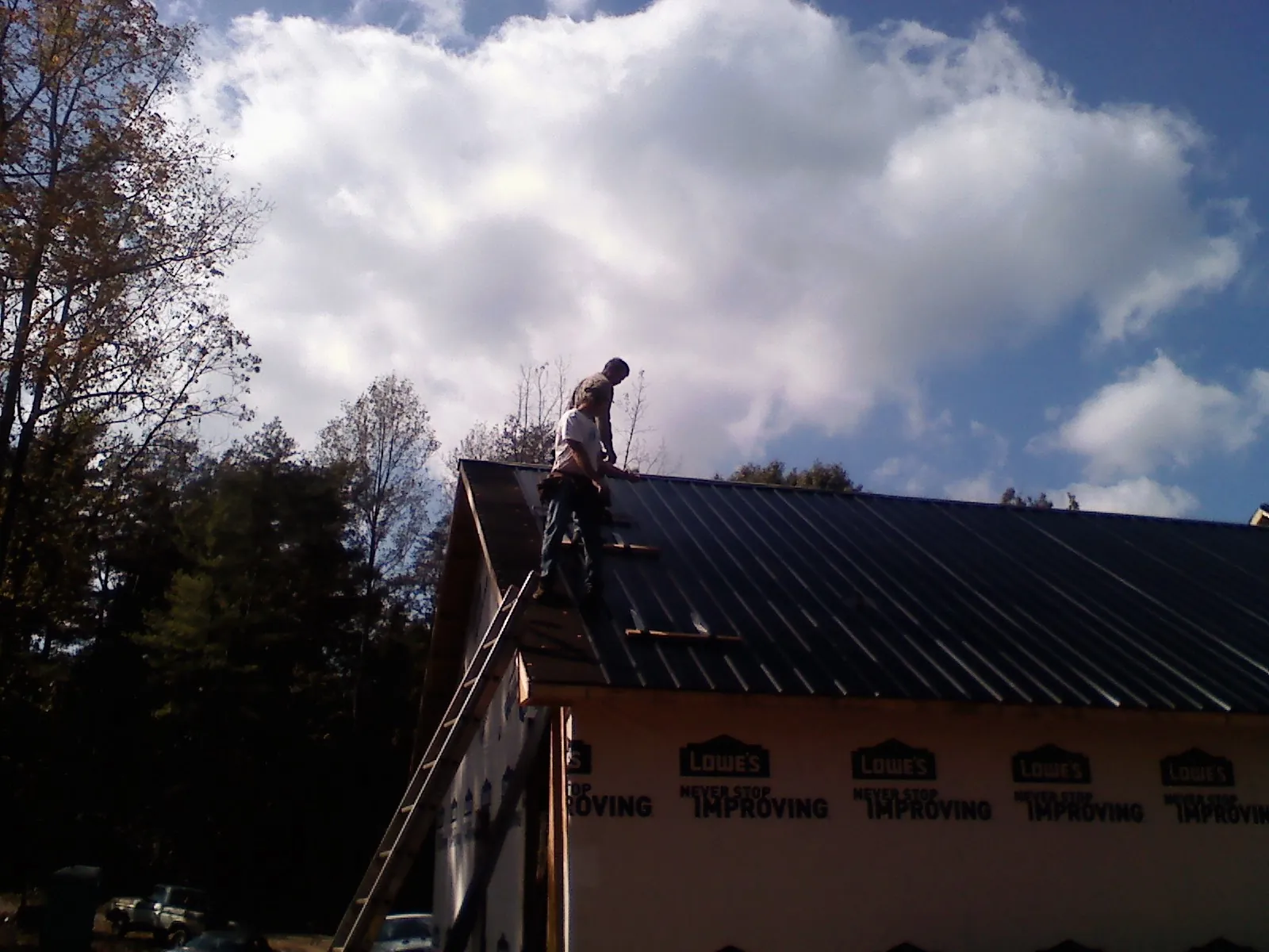 Roofer fastening dark metal panels high against a cloudy sky, from a Roof Inspection job in Cross City