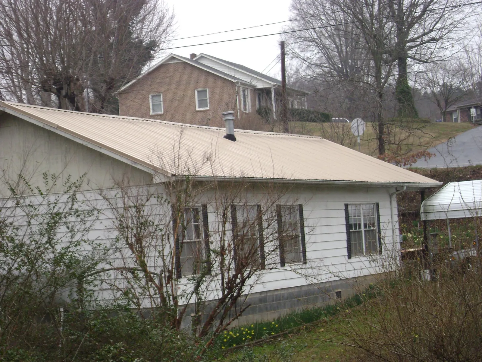 Tan metal roof on a white sided house set into a hillside — Commercial Roofing by Roofing Brothers in Cross City